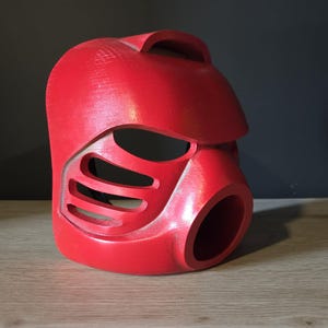 Puede incluir: Un casco r&iacute;gido de color rojo brillante moldeado que presenta una secci&oacute;n superior lisa y redondeada, un borde prominente tipo visera y una serie de tres ranuras de ventilaci&oacute;n horizontales en el lateral. El frente incluye una gran abertura circular.