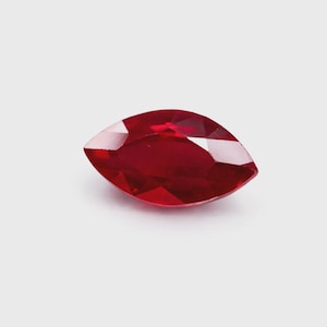 Peut inclure: Un rubis taillé en marquise, d'une couleur rouge profond. La pierre précieuse est facettée, reflétant la lumière et mettant en valeur ses surfaces polies. La forme est allongée avec des extrémités pointues, pour la joaillerie.