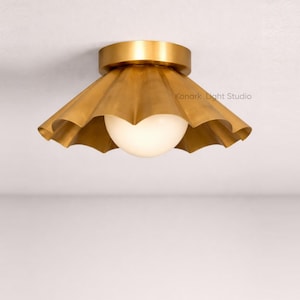 May include: A gold-coloured ceiling light with a ruffled shade and a spherical, frosted glass globe. The fixture is mounted on a white ceiling. The text "Konark Light Studio" is visible on the shade.