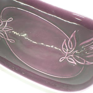 May include: A rectangular, purple-colored dish with a glossy finish. The dish features a decorative floral design in a lighter shade of purple. The design is composed of curved lines and leaf-like shapes.