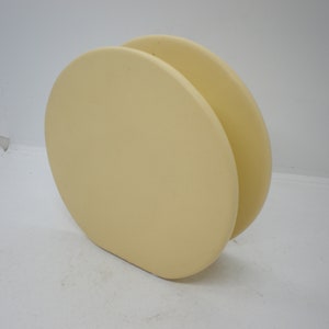 May include: A pale yellow ceramic vase with a rounded, almost circular shape. The vase is made of two pieces that are joined together.