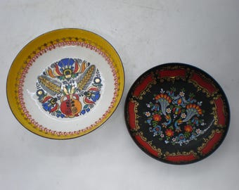 May include: Two decorative plates with floral designs. One plate has a white center with a yellow rim and a colorful floral pattern. The other plate is black with a red border and a floral design.