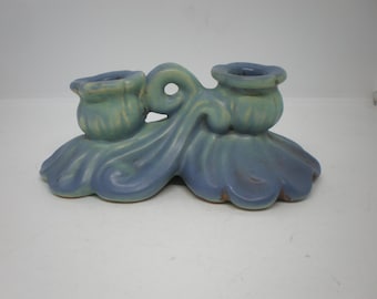 May include: A blue and green ceramic candle holder with two candle cups. The holder is shaped like a stylized flower with a wavy design.