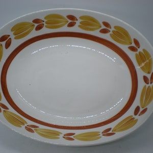 May include: Oval white serving platter with a brown border and a repeating pattern of yellow and brown stylized floral designs around the rim. The platter is empty and has a glossy finish.