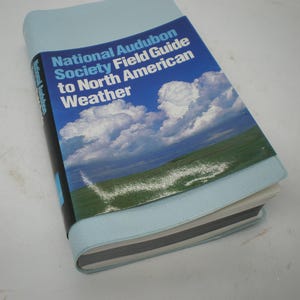 May include: A National Audubon Society Field Guide to North American Weather book. The cover features a blue sky with white clouds and a green field. The book is bound in light blue.