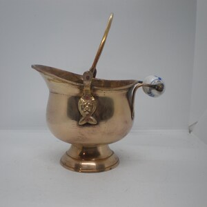 May include: A small, gold-colored metal bucket with a porcelain handle. The bucket has a decorative fish design on the side.
