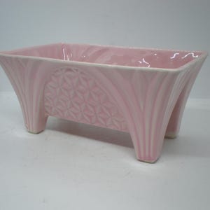 May include: A pink ceramic planter with a geometric design and four legs.