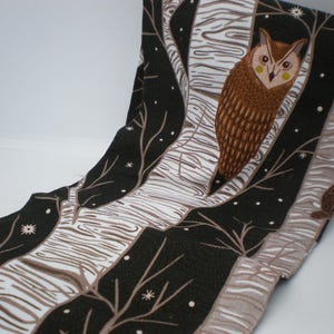 May include: Fabric with a repeating pattern of owls, trees, and stars. The owls are brown with yellow accents, set against a backdrop of black and white tree trunks. The fabric has a whimsical, nature-inspired design.