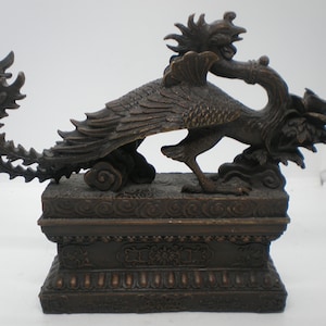 May include: A bronze sculpture of a mythical bird with a long, leafy tail, perched on a decorative base. The bird is depicted with intricate details and a fierce expression.