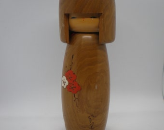 Puede incluir: Muñeca Kokeshi de madera con cabeza redondeada y cuerpo cilíndrico. La muñeca tiene una cara pintada y un diseño floral en rojo y blanco. La muñeca está hecha de madera y tiene un acabado natural.