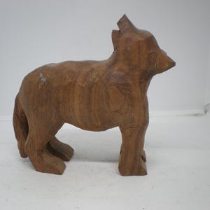 May include: A hand-carved wooden wolf figurine in a standing pose. The sculpture is made of a light brown wood with visible grain and a slightly weathered appearance. The wolf has a detailed form with a pointed snout and upright ears.