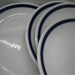 May include: Four white ceramic plates with a blue rim stacked on top of each other.