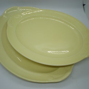 May include: Two pale yellow oval ceramic serving platters with a decorative raised rim and a scalloped edge.