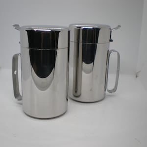 May include: Two silver stainless steel oil or vinegar cruets with lids and handles.