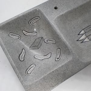 May include: A gray rectangular tray with two compartments. One side features pencil illustrations, the other has drawings of paperclips and an eraser. The tray is speckled with a textured surface.