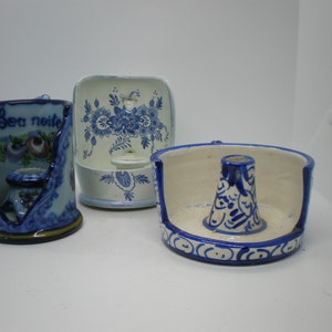 May include: Three ceramic candle holders in blue and white. One has the words "Boa noite" and floral designs. Another is square with floral patterns. The third is round with a central cone-shaped holder and decorative blue patterns.