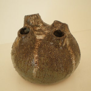May include: A green and brown ceramic vase with three openings. The vase has a rough, textured surface.