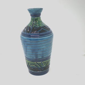 May include: A ceramic vase with a blue, green, and dark blue color scheme. The vase has a textured, ribbed design on the body and decorative leaf patterns. The vase is approximately 10 inches tall.