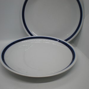 May include: Two white ceramic plates with a single blue band around the rim.