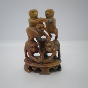 May include: A hand-carved stone sculpture of five monkeys stacked on top of each other. The monkeys are brown and tan in color and have detailed features. The sculpture is on a small, round base.
