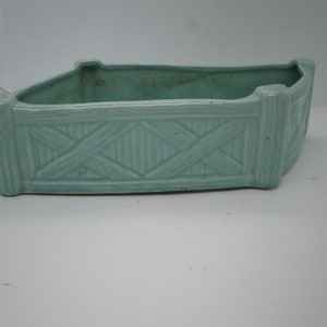 May include: A light blue ceramic planter with a woven design. The planter is rectangular with rounded corners.