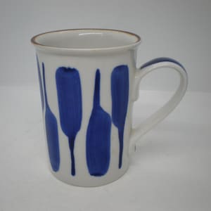 May include: A white ceramic mug featuring a repeating pattern of vertical, hand-painted blue brushstrokes. The mug has a cylindrical body, a curved handle on the right side, and a thin brown rim around the top edge of the vessel.
