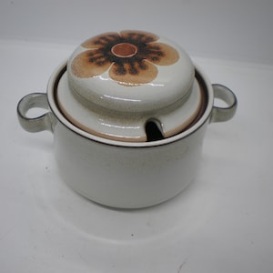 May include: A white ceramic soup tureen with a brown and orange floral design on the lid. The tureen has two handles and a spout on the lid.