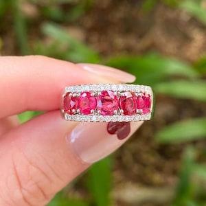 Op de afbeelding: Een zilveren ring met vijf ovale, helder roze edelstenen in een rij. De edelstenen zijn omgeven door een halo van kleine, sprankelende witte diamanten. Een fijn sieraad.
