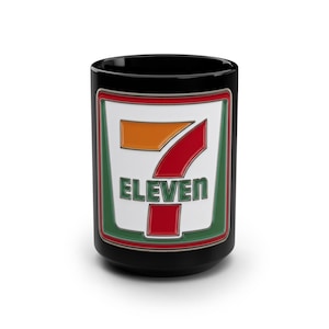May include: Black ceramic mug featuring the "7-Eleven" logo. The logo is a rectangle with a white background, green border, and red and orange accents. The word "ELEVEN" is in green block letters.