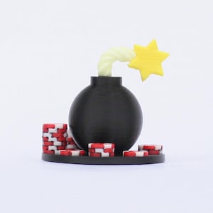 May include: A black bomb figurine with a yellow star and a white fuse. The bomb is surrounded by red, white, and black poker chips, all set against a white background. The design is whimsical and playful.