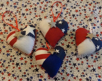 May include: Four felt heart ornaments decorated with red, white, and blue fabric in a patriotic theme. Each heart has a silver star sewn on the front.