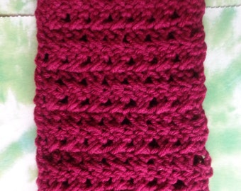 May include: A close-up of a burgundy crocheted scarf with a textured pattern.