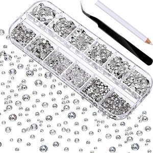May include: A clear plastic organizer filled with various sizes of silver rhinestones. A black tweezer and a white pencil are next to the organizer. Loose rhinestones are scattered around the organizer, creating a sparkling effect. Ideal for nail art and crafts.