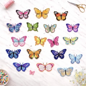 May include: A collection of colorful butterfly patches in various sizes and designs. The patches feature a range of colors, including pink, yellow, blue, green, and orange. A spool of pink thread and a pair of gold scissors are also visible.
