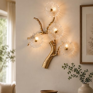 May include: A wall-mounted light fitting featuring a textured gold-toned branch structure with four circular, clear, ribbed glass shades. Each shade is illuminated from the centre by a warm light, creating a glowing effect against the wall surface.