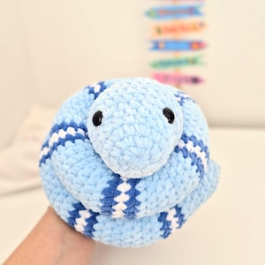 Peut inclure: Un jouet serpent bleu crocheté avec des rayures blanches et bleu foncé. Le serpent a des yeux noirs et est enroulé. Le jouet en peluche est fait de fil doux et texturé.