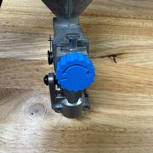 May include: A metal reloading tool with a blue adjustment knob. The tool has a funnel-shaped top and a lever mechanism. The blue knob is textured and has directional markings. The tool is designed for reloading ammunition.