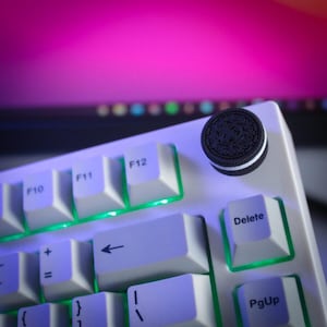 May include: A white mechanical keyboard with light-up green edges and white keycaps. An Oreo cookie sits on the top right corner. The background is a blurred display with pink and purple hues.