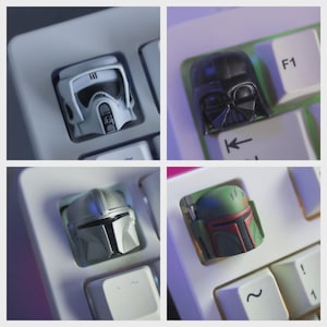 Puede incluir: Cuatro teclas personalizadas con personajes de Star Wars: un casco blanco de Scout Trooper, el casco de Darth Vader, un casco mandaloriano y el casco de Boba Fett. Las teclas están en un teclado blanco.