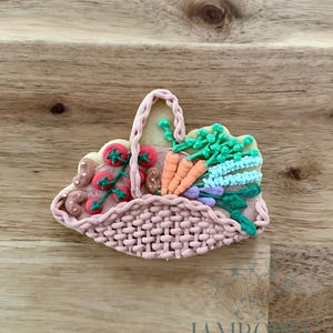 Pode incluir: Um biscoito de açúcar decorado em forma de cesta tecida, cheio de vegetais coloridos. O biscoito apresenta tomates vermelhos, cenouras laranjas, ervas verdes e detalhes roxos, tudo meticulosamente elaborado com glacê.