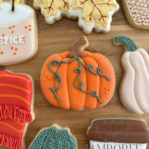 May include: An assortment of decorated sugar cookies with a fall theme. The cookies include a pumpkin, leaves, a sweater, a candle, and a coffee cup. The cookies are decorated with orange, yellow, green, and brown icing.