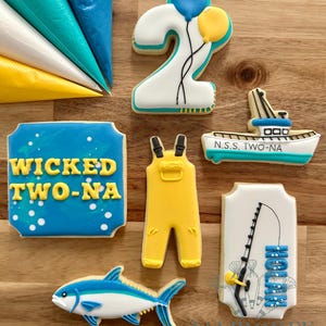Puede incluir: Una colección de galletas de azúcar decoradas con temática náutica. Las galletas incluyen un número 2 con globos, un barco, un pez, un mono y un letrero que dice "Wicked Two-Na". Las galletas están decoradas con glaseado azul, amarillo y blanco.