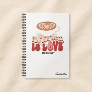May include: White spiral-bound notebook with the text "ALL YOU NEED IS LOVE AND COFFEE" in a retro font. A coffee cup with a heart design is above the text. The name "Samantha" is printed at the bottom.
