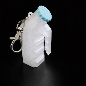 May include: A clear, 3D-printed keychain shaped like a small milk jug with a light blue cap. The keychain has a silver clasp for attaching to keys or bags. The design includes a handle and a textured body, set against a black background.