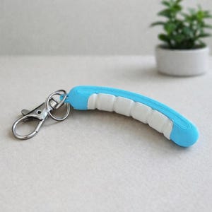 May include: A blue and white keychain with a silver clasp. The curved handle is light blue with white sections. The keychain is on a light-colored surface.