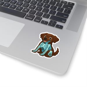 May include: A brown sticker featuring a cartoon dog with a blue skeleton design. The dog is smiling with its tongue out. The sticker is placed on a laptop.