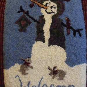 Puede incluir: Una alfombra azul y blanca con un dise&ntilde;o de mu&ntilde;eco de nieve. El mu&ntilde;eco de nieve lleva un sombrero verde y morado y tiene una nariz de zanahoria. La alfombra tiene la palabra "Bienvenido" escrita en ella.