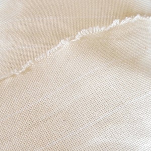 Puede incluir: Primer plano de un trozo de tela de color blanco roto con textura tejida. La tela tiene un borde sin rematar.