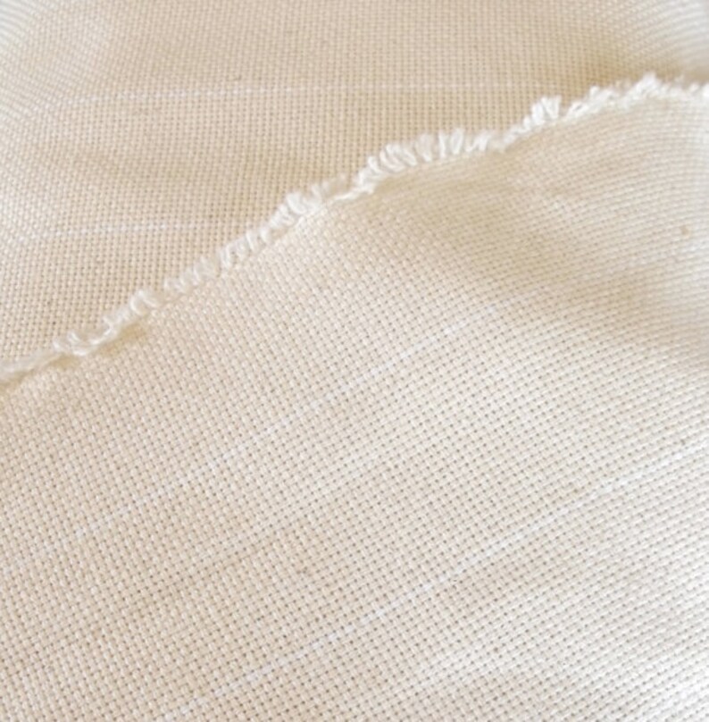 Puede incluir: Primer plano de un trozo de tela de color blanco roto con textura tejida. La tela tiene un borde sin rematar.