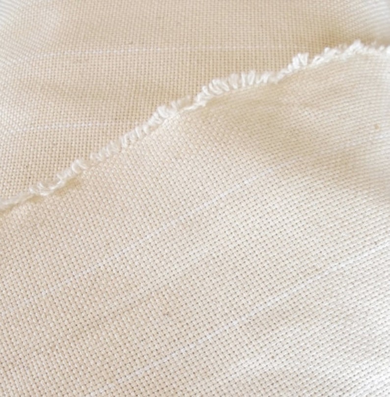 May include: Close-up of a piece of off-white fabric with a woven texture. The fabric has a raw edge.